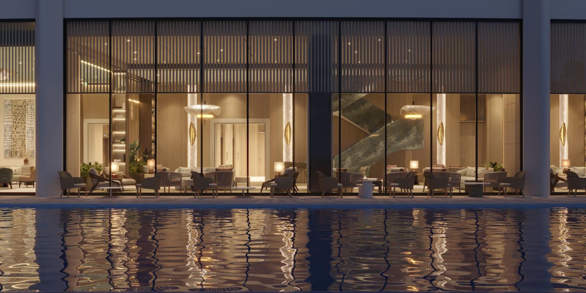 Glass-fronted lounge at Shang Bauhinia Residences with warm interiors, elegant seating, and poolside reflections
